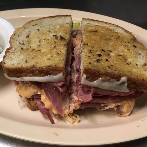 A large reuben sandwich, cut in half, with corned beef, sauerkraut, cheese, and dressing.