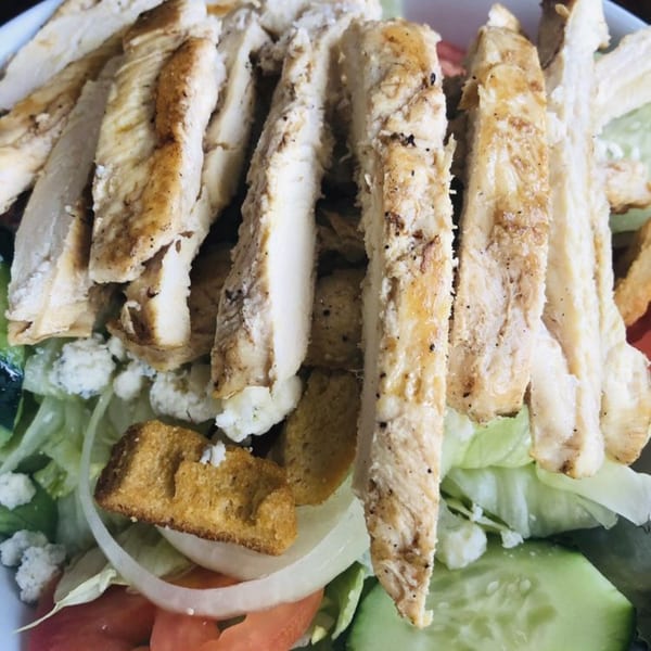 Close-up of a grilled chicken salad with lettuce, tomatoes, cucumbers, onions, croutons, and blue cheese.