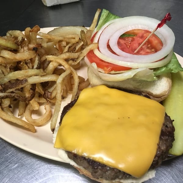 Cheeseburger with lettuce, tomato, onion, curly fries, and a pickle spear on a plate.